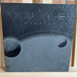 May include: A black and white image of a record album cover with the title "Dune Imperium" in white text. The album cover features a black and white image of a planet with rings.