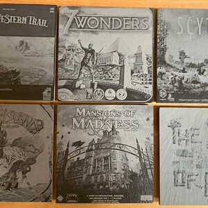 May include: A collection of six board game boxes with black and white images. The games are: Great Western Trail, 7 Wonders, Scythe, Spirit Island, Mansions of Madness, and The Isle of Cats.