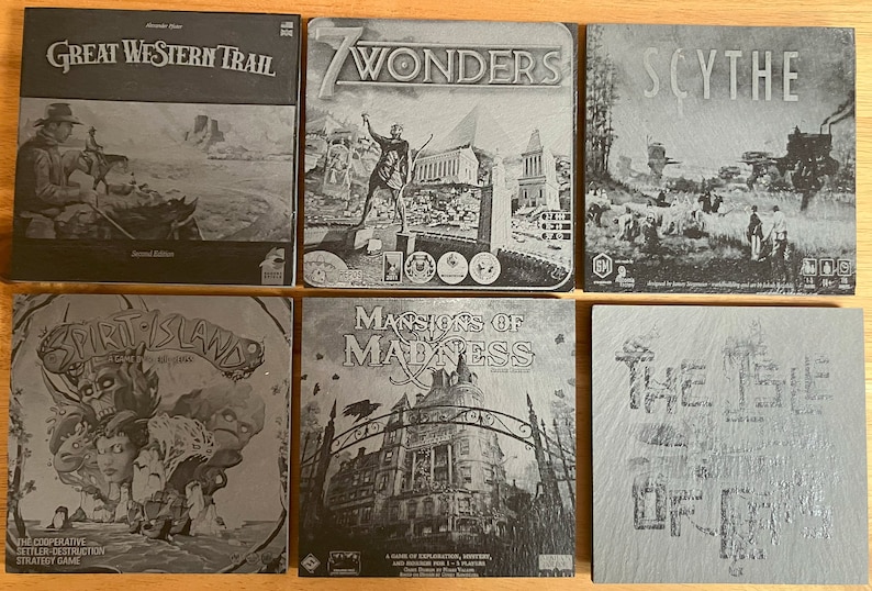 May include: A collection of six board game boxes with black and white images. The games are: Great Western Trail, 7 Wonders, Scythe, Spirit Island, Mansions of Madness, and The Isle of Cats.