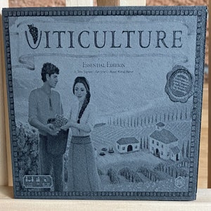 May include: A black and white image of a board game box with the title "VITICULTURE ESSENTIAL EDITION" printed on the front. The box features a couple standing in a vineyard with a small village in the background.
