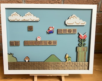 May include: A framed 3D pixel art scene of a classic video game level. The scene features a green hill, a brown pipe, a red flower, a mushroom, and two characters: Mario and a turtle. The characters are made of wood and are raised from the background.