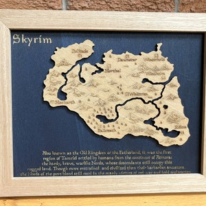 May include: A framed wooden map of Skyrim, a fictional province from the video game The Elder Scrolls V: Skyrim. The map is on a dark blue background and includes the names of various locations within the province, such as "Whiterun", "Markarth", and "Dawnstar". The text below the map reads: "Also known as the Old Kingdom or the Fatherland, it was the first region of Tamriel settled by humans from the continent of Atmora: the hardy, brave, warlike Nords, whose descendants still occupy this rugged land. Though more restrained and civilised than their barbarian ancestors, the Lords of the pure blood still excel in the manly virtues of red war and bold exploration."