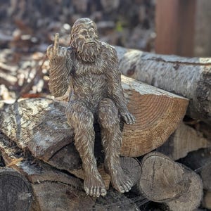 May include: A brown, furry Bigfoot figurine sitting on a pile of logs. The figurine is giving the middle finger.
