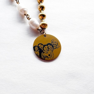 May include: A necklace featuring a gold-colored pendant with a black engraved family portrait. The necklace has a strand of white pearls and gold-colored beads. The pendant is round and has a yellow background.