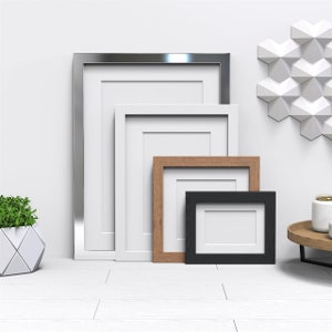 May include: Four picture frames of different sizes and colours, arranged in a row on a white surface. The frames are silver, white, brown, and black.