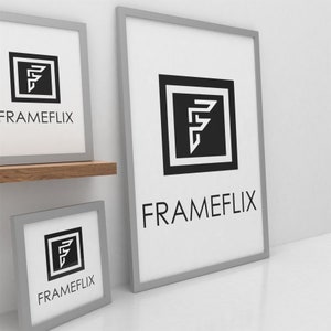 May include: Three silver picture frames with white mounts and black and white graphic designs. The largest frame has the text "FRAMEFLIX" and a stylised "F" logo. The smaller frames have the same logo and text.