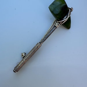 May include: A green jade stone axe head wrapped in silver wire, attached to a silver spring coil.