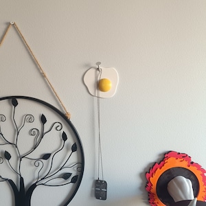 May include: A white ceramic egg-shaped wall hook with a yellow yolk, a black metal tree wall decor, and a red and orange fire-shaped wall decor with a black circle in the center.