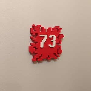 Op de afbeelding: Een rood gepixelde huisnummerbord met het nummer 73 in wit.