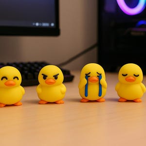Peut inclure: Quatre figurines de canard en caoutchouc jaune avec différentes expressions faciales : heureux, en colère, en pleurs et endormi. Chaque canard a un bec et des pieds orange. Les figurines sont disposées en rangée sur une surface marron clair.