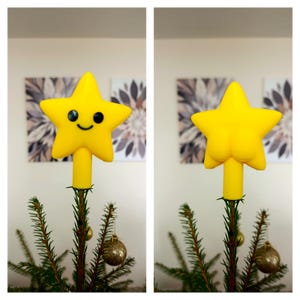Op de afbeelding: Een heldergele ster voor op de kerstboom met een lachend gezicht, zwarte ogen en een gebogen mond. De ster is gemonteerd op een gele steel en staat op een kerstboom met gouden ornamenten.