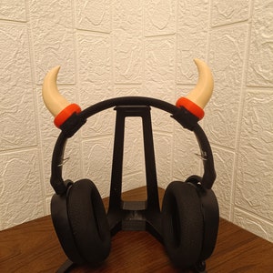 Puede incluir: Auriculares negros con un soporte negro y dos cuernos blancos con detalles naranjas en la diadema.