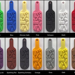 May include: A collection of fourteen rectangular key tags with rounded ends and a hole at the top. Each tag features a raised pattern of small building blocks on the surface. The tags are available in green, blue, yellow, pink, black, white, red, purple, brown, orange, gray, and sparkling finishes.