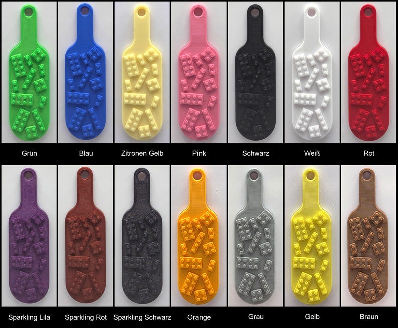 May include: A collection of fourteen rectangular key tags with rounded ends and a hole at the top. Each tag features a raised pattern of small building blocks on the surface. The tags are available in green, blue, yellow, pink, black, white, red, purple, brown, orange, gray, and sparkling finishes.
