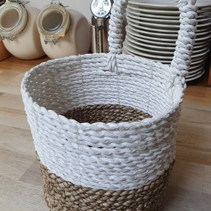 May include: A white and brown woven storage basket with a rope handle. The basket is made of natural materials and has a rustic look.