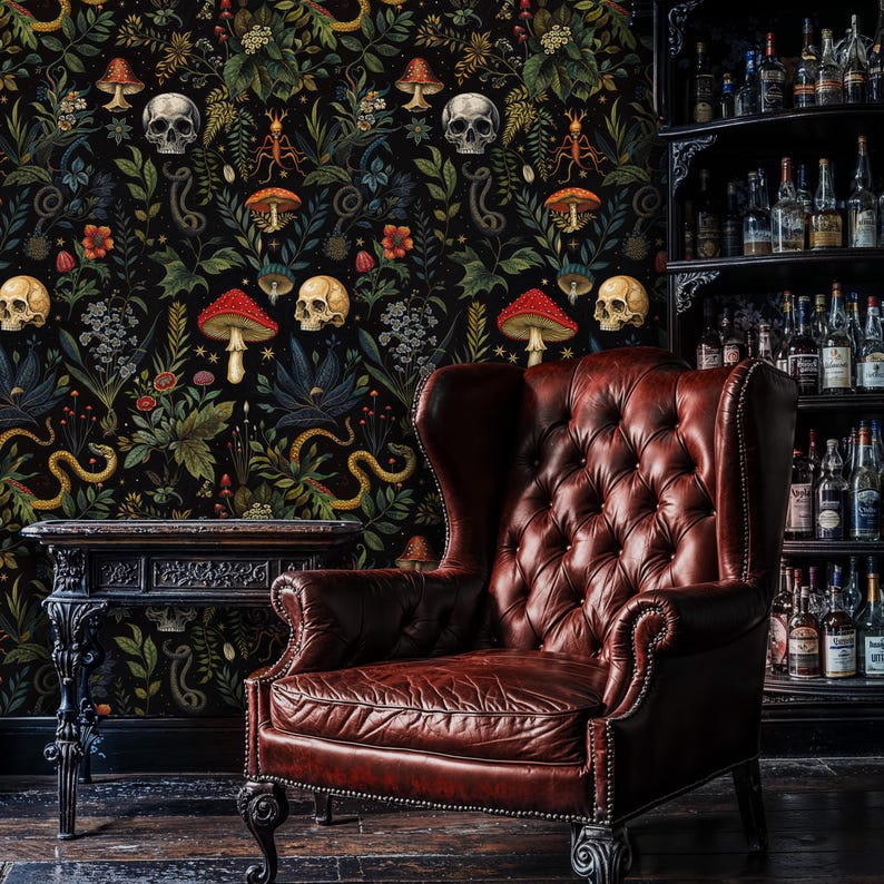 Op de afbeelding: Een donkerrode leren fauteuil met knopen zit voor een zwarte behang met een botanisch en schedelpatroon. Het behang heeft rode paddenstoelen, slangen en schedels.