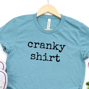 May include: A teal blue t-shirt with the text "cranky shirt" printed in black.