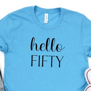 May include: A light blue t-shirt with the text "hello FIFTY" in black lettering.