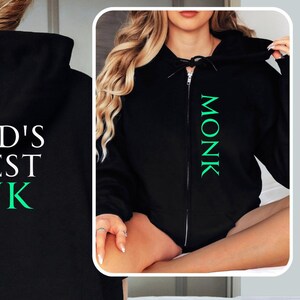 Puede incluir: Sudadera con capucha negra con un gráfico verde y amarillo que dice "World's Okayest Monk".