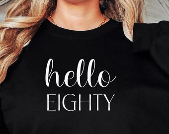 May include: Black sweatshirt with the text "hello eighty" in white lettering.
