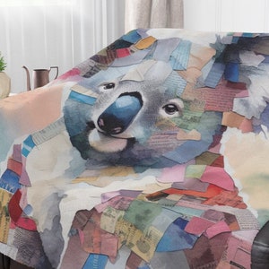 May include: A soft throw blanket featuring a koala illustration composed of a collage of colorful paper scraps, including various shades of blue, pink, red, and green, with visible printed text fragments layered throughout the design.