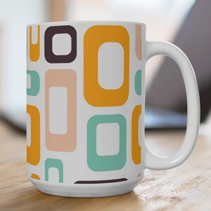 May include: White ceramic mug with a retro geometric pattern in shades of brown, orange, teal, and peach. The mug has a large handle and a cylindrical shape, perfect for coffee or tea.