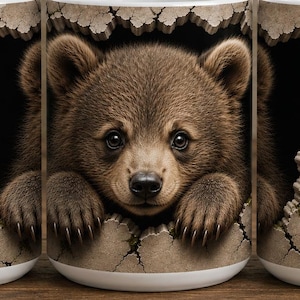 Peut inclure: Un mug en céramique blanche présentant un motif à effet 3D d'un ourson brun regardant à travers un mur de pierre fissuré. L'ours est entouré de fougères vertes, de fleurs sauvages violettes et de mûres. Le mug est montré sous trois angles.