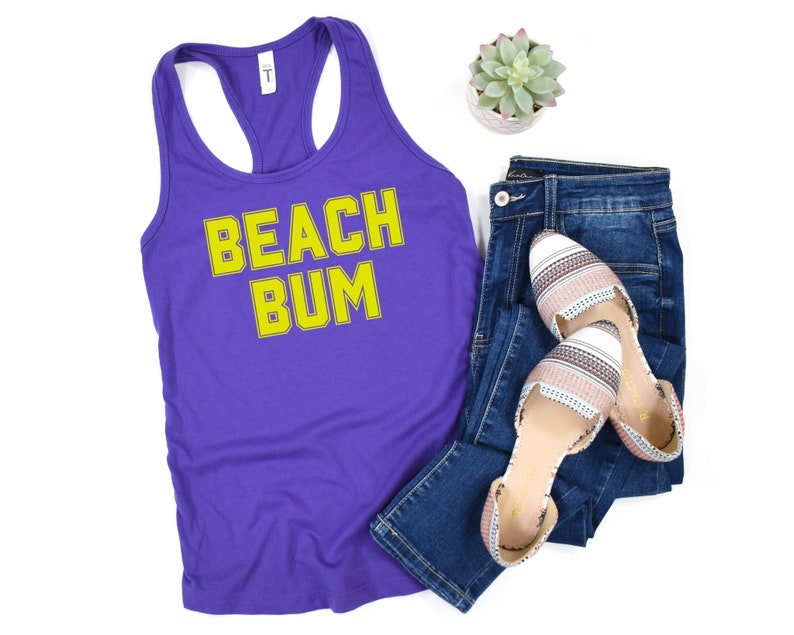 May include: Purple tank top with the text "BEACH BUM" in yellow outlined letters. The tank top is paired with blue jeans and white and pink striped flats.