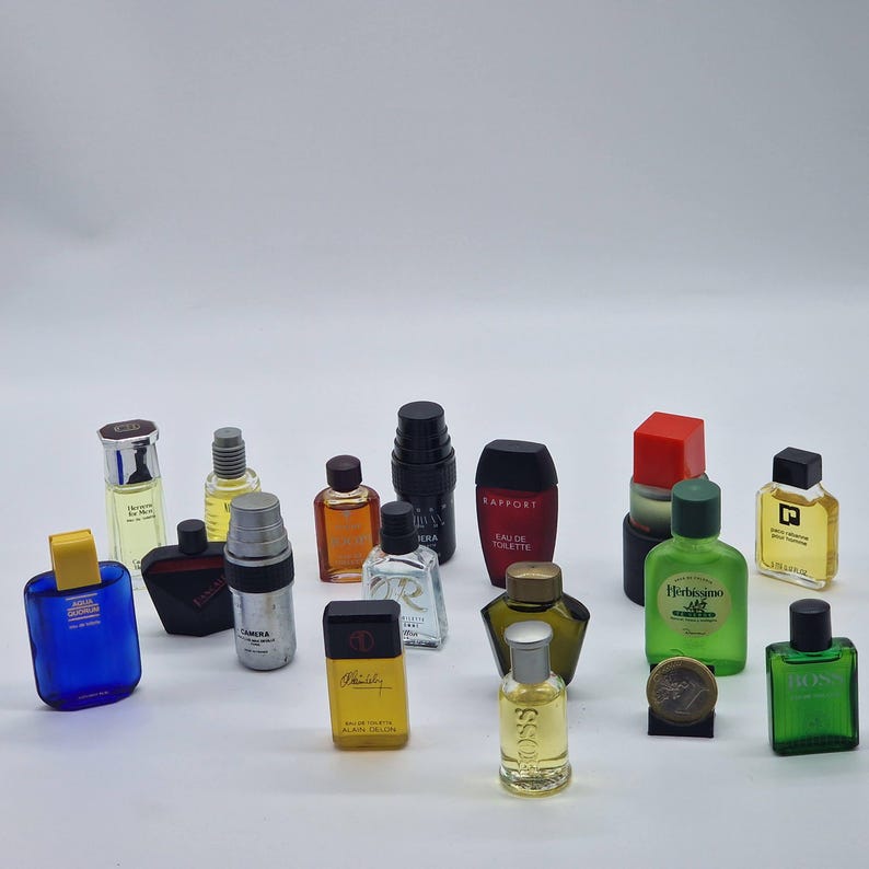 May include: A collection of miniature perfume bottles in various shapes and colors. The bottles include blue, green, red, and yellow, with different cap designs. Some bottles have labels with text.