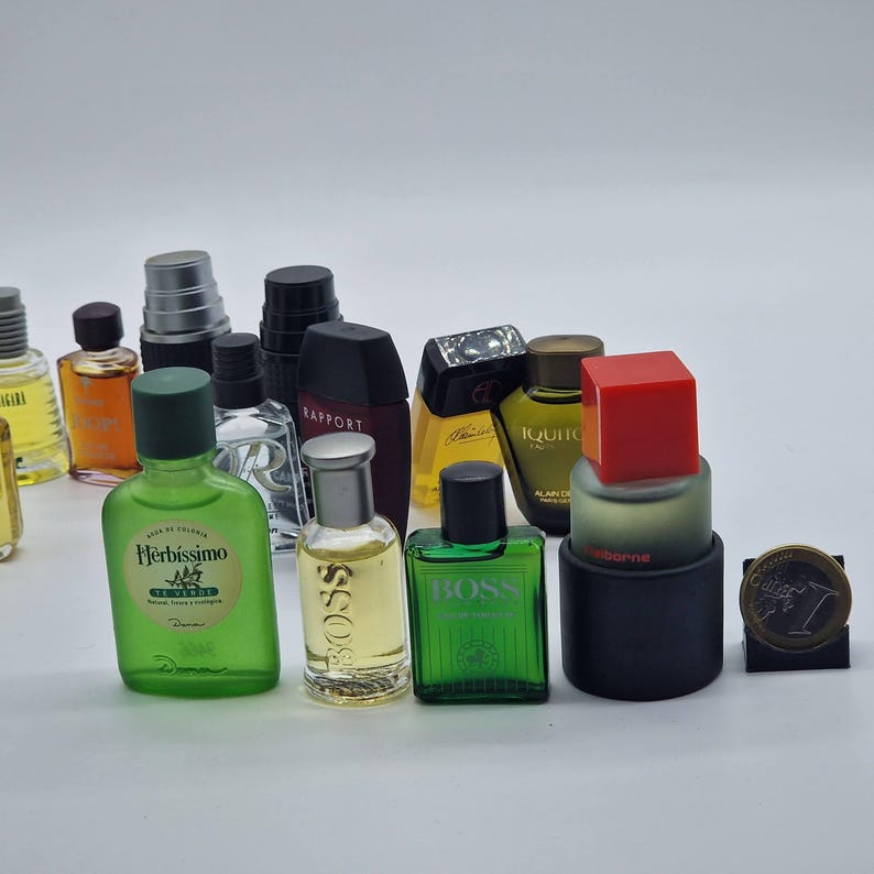 May include: A collection of miniature perfume and cologne bottles in various shapes, sizes, and colors. The bottles include green, clear, and black glass, with silver, black, and red caps. Some bottles have labels with text.