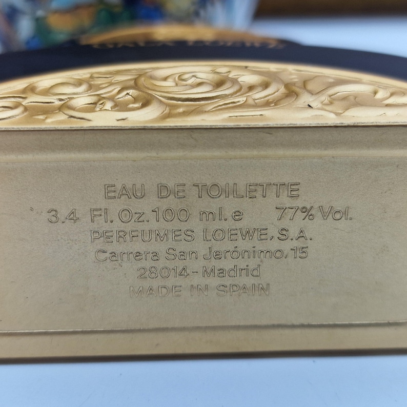 May include: A rectangular perfume bottle with the text "EAU DE TOILETTE" and "3.4 Fl. Oz. 100 ml.e 77% Vol." printed on the front. The bottle is labeled "PERFUMES LOEWE, S.A." and "MADE IN SPAIN". The top of the bottle has a decorative gold design.