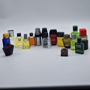 May include: A collection of miniature perfume bottles in various shapes, sizes, and colors. The bottles include clear, black, red, green, and yellow designs. Some bottles have labels, and a small, round, bronze-colored item is in the center.