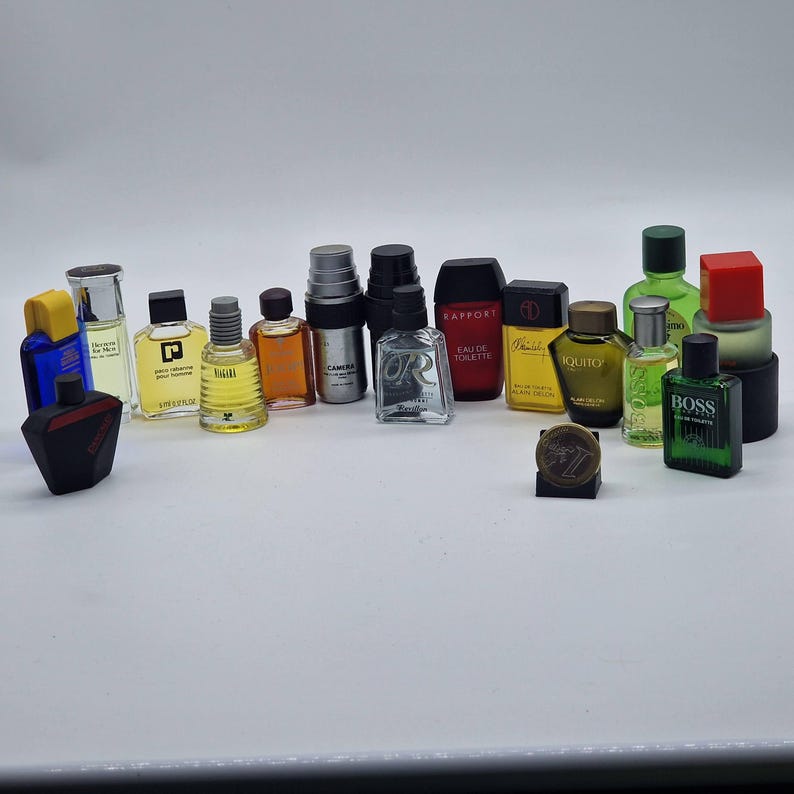 May include: A collection of miniature perfume bottles in various shapes, sizes, and colors. The bottles include clear, black, red, green, and yellow designs. Some bottles have labels, and a small, round, bronze-colored item is in the center.