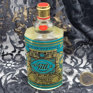 May include: A vintage bottle of "Echt K&ouml;lnisch Wasser" cologne. The label features teal and gold accents with the number "4711". The bottle has a gold cap with a red seal. The text "Original Eau de Cologne" is visible.