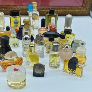 K&ouml;nnte beinhalten: Eine Sammlung von Miniatur-Parf&uuml;mflaschen in verschiedenen Formen und Gr&ouml;&szlig;en. Die Flaschen sind mit farbigen Fl&uuml;ssigkeiten gef&uuml;llt und weisen unterschiedliche Verschlussdesigns auf. Einige Flaschen sind beschriftet, und eine M&uuml;nze ist ebenfalls vorhanden.