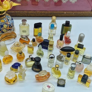 K&ouml;nnte beinhalten: Eine Sammlung von Miniatur-Parf&uuml;mflaschen in verschiedenen Formen und Gr&ouml;&szlig;en. Die Flaschen sind mit unterschiedlich farbigen Fl&uuml;ssigkeiten gef&uuml;llt und haben eine Vielzahl von Verschl&uuml;ssen und Designs. Einige Flaschen sind klar, andere farbig.