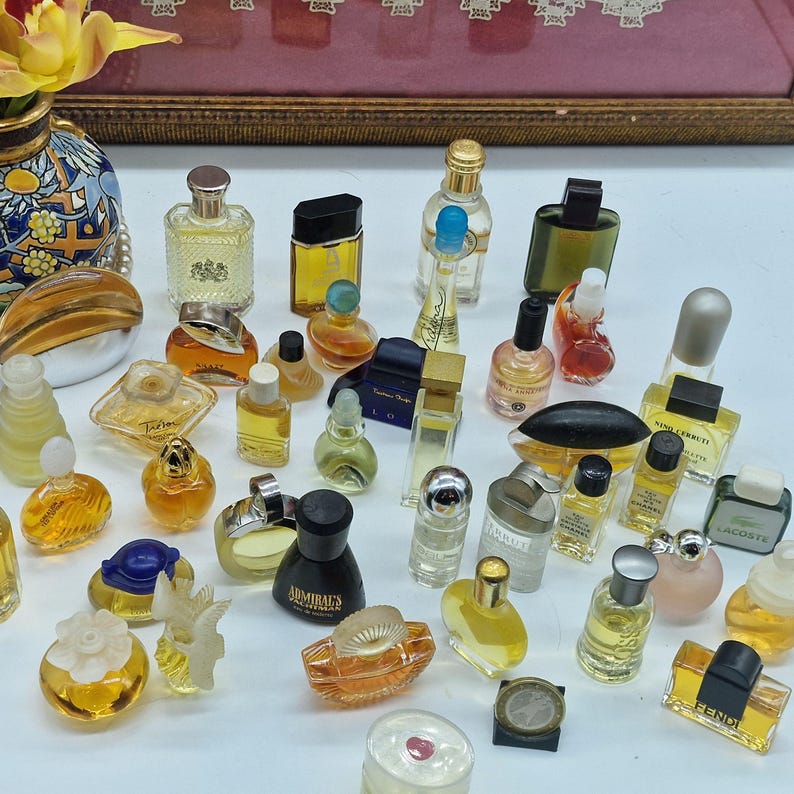 K&ouml;nnte beinhalten: Eine Sammlung von Miniatur-Parf&uuml;mflaschen in verschiedenen Formen und Gr&ouml;&szlig;en. Die Flaschen sind mit unterschiedlich farbigen Fl&uuml;ssigkeiten gef&uuml;llt und haben eine Vielzahl von Verschl&uuml;ssen und Designs. Einige Flaschen sind klar, andere farbig.