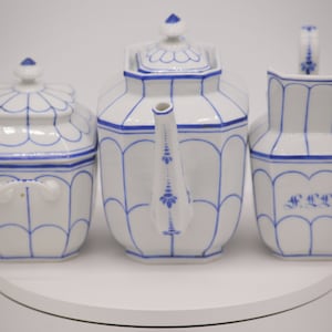 Könnte beinhalten: Ein weißes Porzellan-Tee-Set mit blauen und weißen Blumenmustern. Das Set enthält eine Teekanne, eine Milchkännchen und eine Zuckerdose.