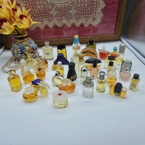 K&ouml;nnte beinhalten: Eine Sammlung von Miniatur-Parf&uuml;mflaschen in verschiedenen Formen und Gr&ouml;&szlig;en. Die Flaschen sind klar, bernsteinfarben und farbig, mit einer Vielzahl von Verschl&uuml;ssen und Designs. Einige Flaschen haben Etiketten, angeordnet auf einer wei&szlig;en Oberfl&auml;che.