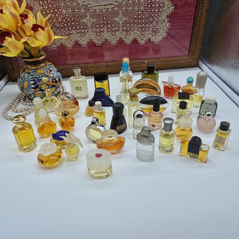 K&ouml;nnte beinhalten: Eine Sammlung von Miniatur-Parf&uuml;mflaschen in verschiedenen Formen und Gr&ouml;&szlig;en. Die Flaschen sind klar, bernsteinfarben und farbig, mit einer Vielzahl von Verschl&uuml;ssen und Designs. Einige Flaschen haben Etiketten, angeordnet auf einer wei&szlig;en Oberfl&auml;che.