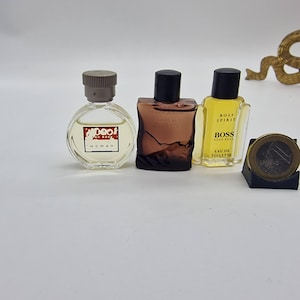 Puede incluir: Tres frascos de perfume en miniatura. Uno es redondo con tapa gris y el texto "Hugo Boss Woman". El segundo es un frasco marrón cuadrado con tapa negra. El tercero es un frasco amarillo con el texto "Boss Spirit" y "Eau de Toilette".