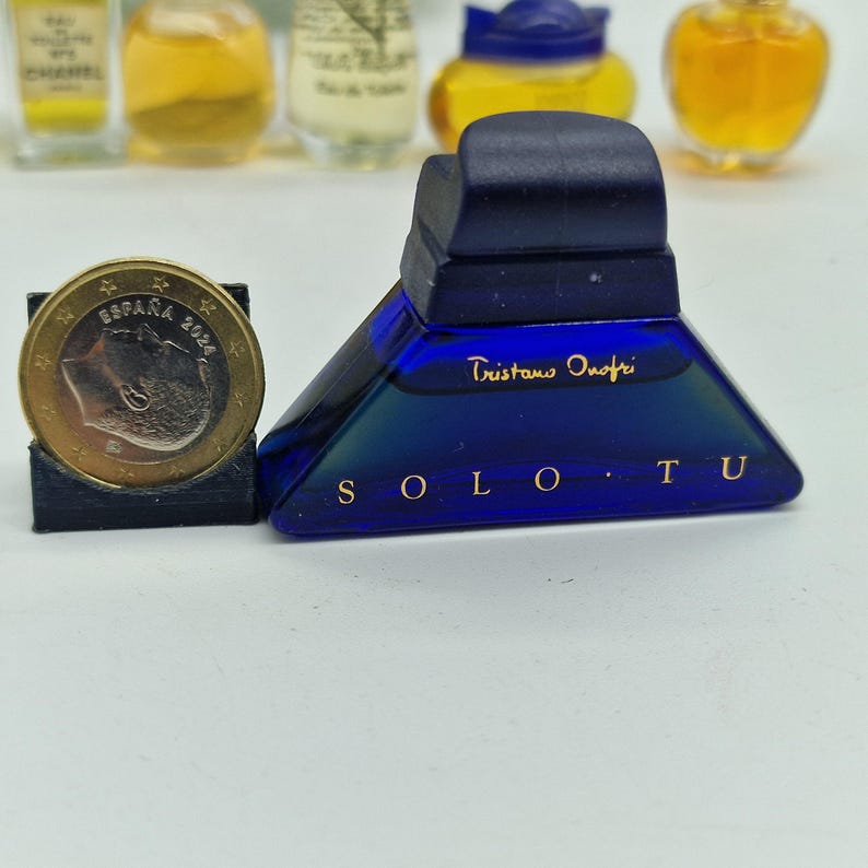 K&ouml;nnte beinhalten: Kleine, dreieckige blaue Parf&uuml;mflasche mit dunkelblauem Deckel. Auf der Flasche stehen die Worte "SOLO TU" und "Tristano Onofri". Eine M&uuml;nze befindet sich neben der Flasche.