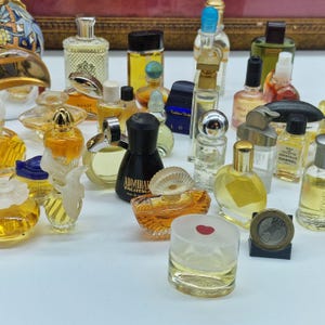 K&ouml;nnte beinhalten: Eine Sammlung von Miniatur-Parf&uuml;mflaschen in verschiedenen Formen und Farben. Die Flaschen bestehen aus Glas und Kunststoff mit einer Vielzahl von Verschl&uuml;ssen und Designs. Einige Flaschen haben Etiketten, und eine M&uuml;nze ist ebenfalls sichtbar.