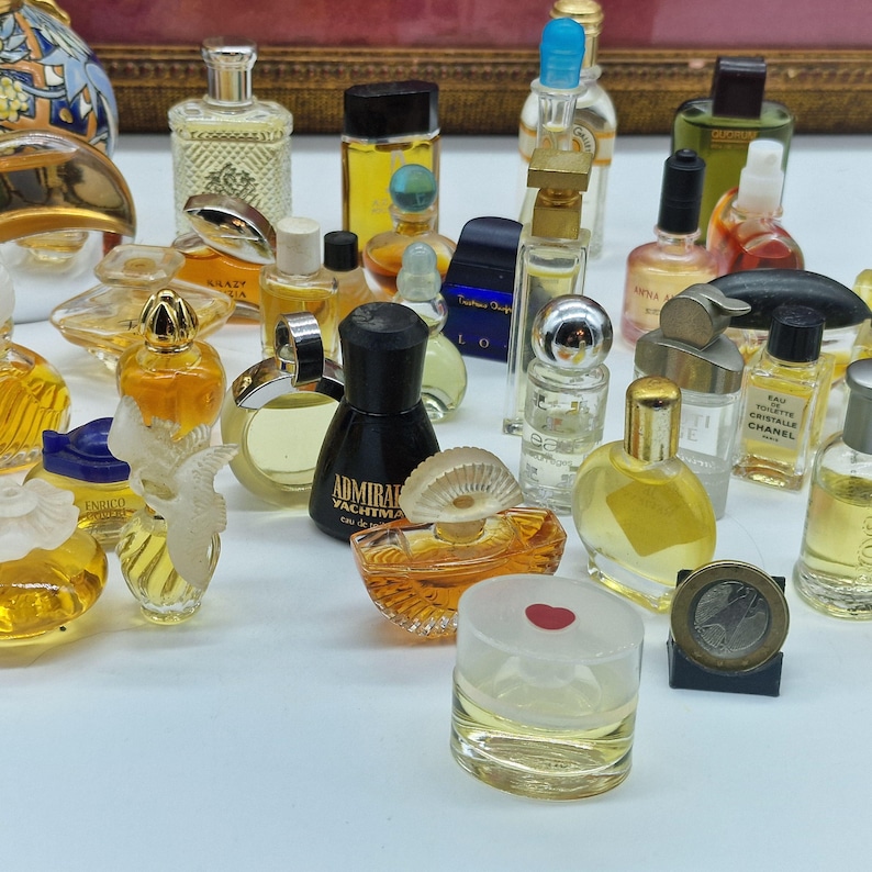 K&ouml;nnte beinhalten: Eine Sammlung von Miniatur-Parf&uuml;mflaschen in verschiedenen Formen und Farben. Die Flaschen bestehen aus Glas und Kunststoff mit einer Vielzahl von Verschl&uuml;ssen und Designs. Einige Flaschen haben Etiketten, und eine M&uuml;nze ist ebenfalls sichtbar.