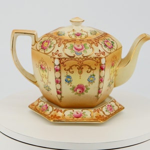 以下が含まれることがあります： ピンク、イエロー、ブルーの花柄と金色のアクセントが施された、ヴィンテージの八角形のティーポットとベース。ベースにも花柄が施されています。
