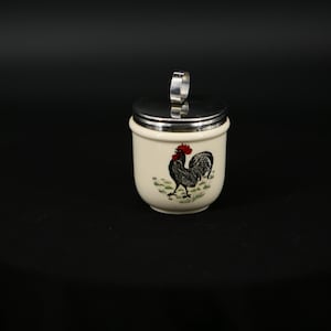 May include: White ceramic egg cup with a silver lid and a rooster design. The rooster is black and white with a red comb.