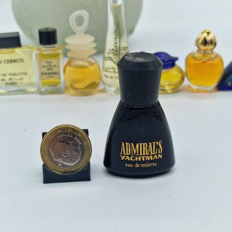 K&ouml;nnte beinhalten: Eine Sammlung von Miniatur-Parf&uuml;mflaschen, darunter eine schwarze Flasche mit der Aufschrift "Admiral's Yachtman eau de toilette". Neben den Parf&uuml;mflaschen liegt eine Euro-M&uuml;nze. Andere Flaschen enthalten gelbe und klare Fl&uuml;ssigkeiten.