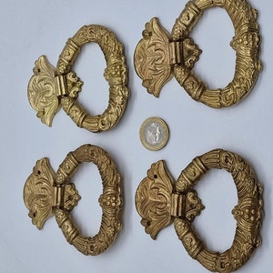 Könnte beinhalten: Vier verzierte goldfarbene Metall-Türgriffe mit aufwendigen floralen Designs. Jeder Griff verfügt über einen ringförmigen Griff und eine dekorative, gerollte Rückplatte.