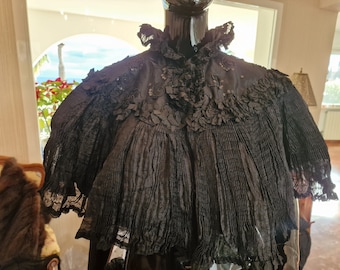 May include: A black lace shawl with a ruffled collar and beaded embellishments. The shawl is pleated and has a sheer, delicate texture.