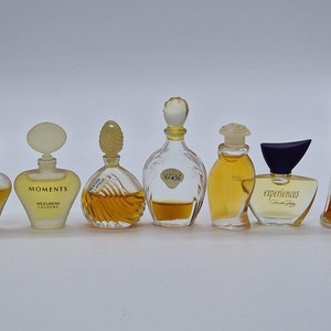 Può includere: Una collezione di otto flaconi di profumo in miniatura con vari design ed etichette. I flaconi sono disposti in fila su una superficie bianca. Le etichette includono "Moments", "Experiences", "Private Number" e "Fleur de Mai".